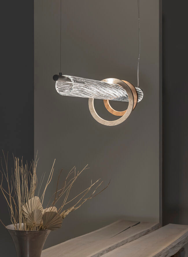 Modern pendant light fixture hanging against a gray wall with a plant and wooden surface in the foreground.