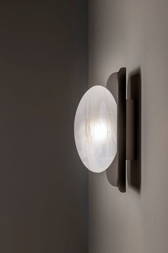Wall-mounted light fixture with a glass shade on a dark background