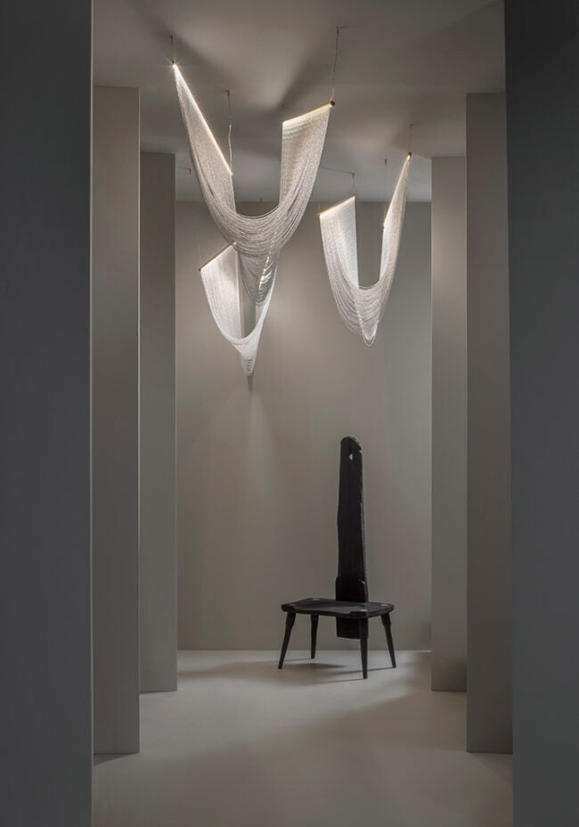 Modern chandelier hanging in a minimalistic room with a black chair.