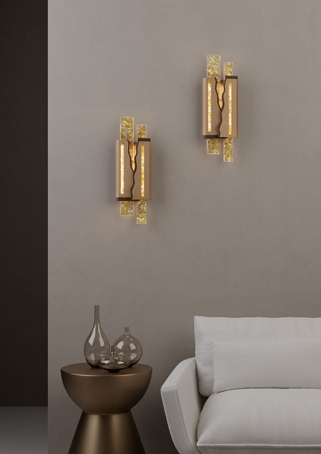 Two gold wall sconces on a gray wall with a side table and sofa in the foreground.