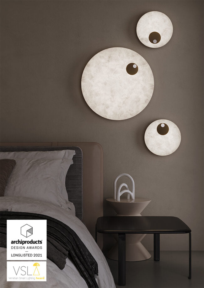 Modern wall lights on a bedroom wall with a bed and nightstand in the foreground.
